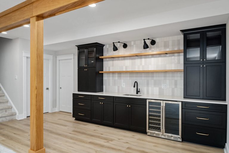 Basement wet bar with black cabinets, wood shelving, and a beverage fridge — MDR Design-Build-Remodel