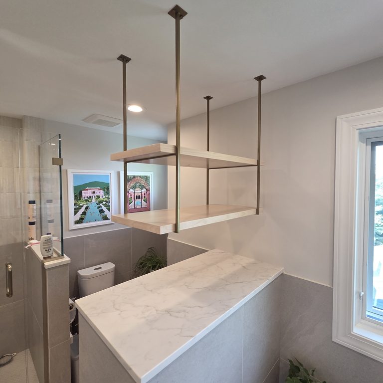 Bathroom with a glass shower, capped half wall and suspended open shelving by MDR Design-Build-Remodel