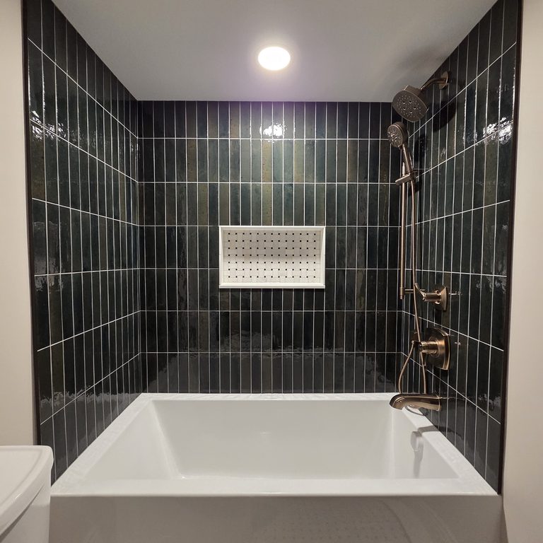Soaking tub surrounded by deep green vertical tile with a patterned niche by MDR Design-Build-Remodel