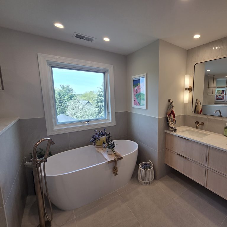Freestanding tub with a floor-mounted filler beside a floating double vanity by MDR Design-Build-Remodel