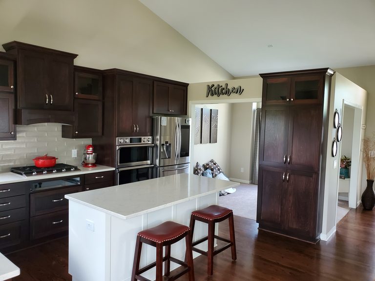 Kitchen with espresso cabinetry, a white island with bar stools and a vaulted ceiling by MDR Design-Build-Remodel